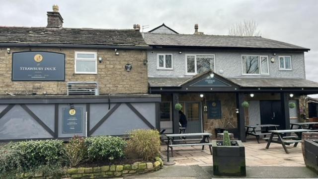 een gebouw met een tafel en banken ervoor bij The Strawbury Duck Inn in Darwen