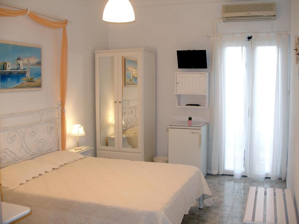 a white bedroom with a bed and a tv at Arethousa in Plaka Milou