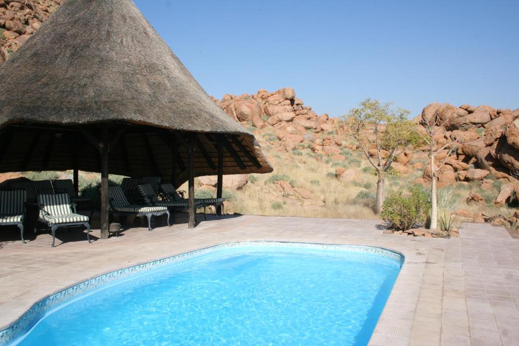 - une piscine avec un parasol et des chaises au toit de chaume dans l'établissement Namib Naukluft Lodge, à Solitaire