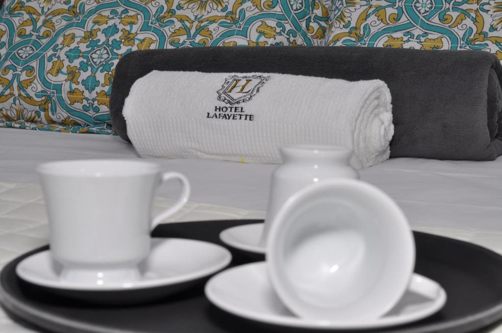 a tray with two cups and saucers on a bed at Hotel Lafayette in Itaquaquecetuba