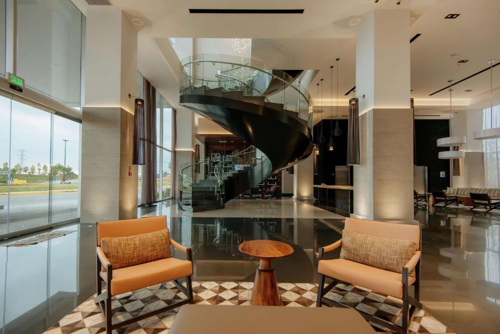 a lobby with two chairs and a glass staircase at Hilton Garden Inn Puebla Angelopolis in Puebla