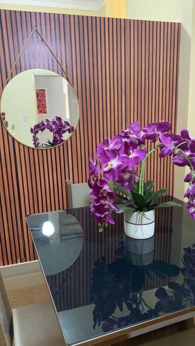 un vaso di fiori viola su un tavolo con uno specchio di Apartamento encantador 04 a Montes Claros