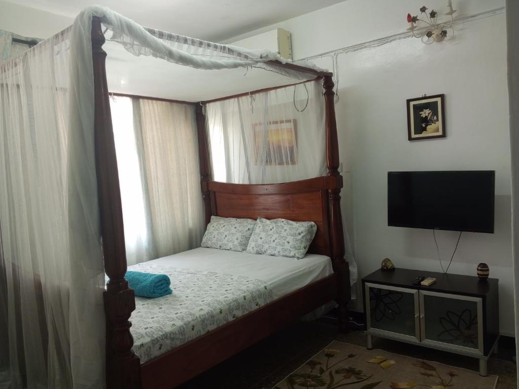 a bedroom with a canopy bed and a television at Paradise Apartment in Mombasa