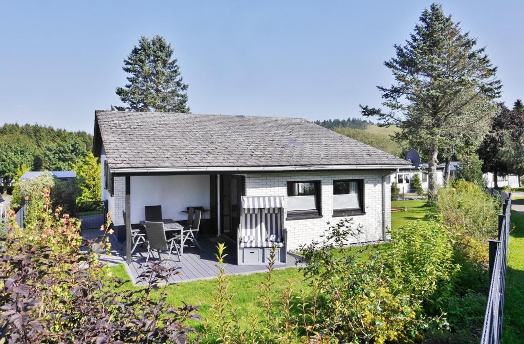 Cabaña blanca con porche y sillas en un patio en Ferienhaus Diemelquelle - ex Ons Huisje 8, en Willingen