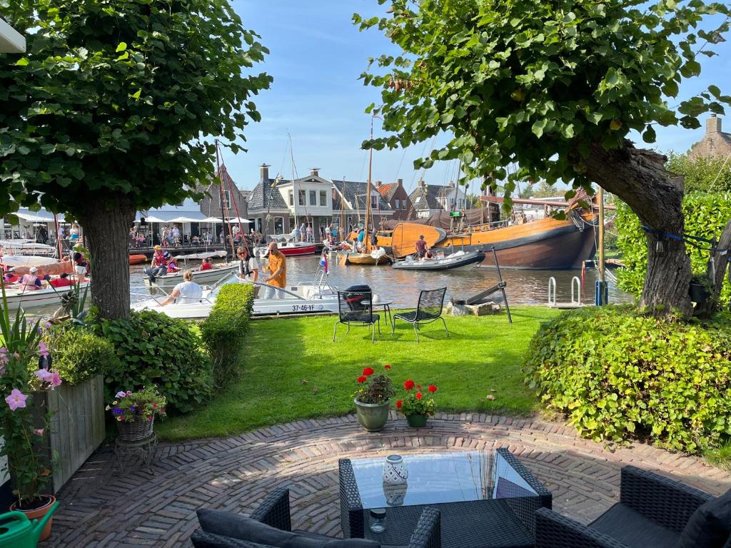 a garden with a table and chairs and boats in the water at It Kapteinshûske in Heeg