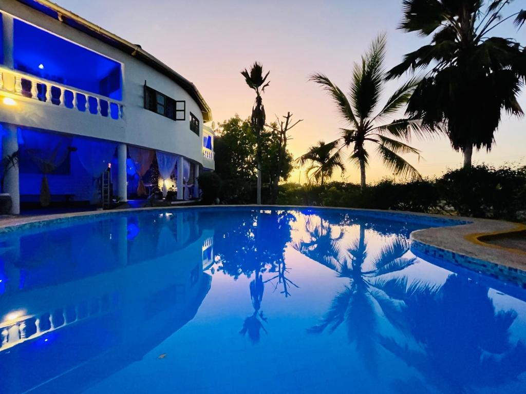a swimming pool in front of a house with palm trees at Casa Hera in Diani Beach