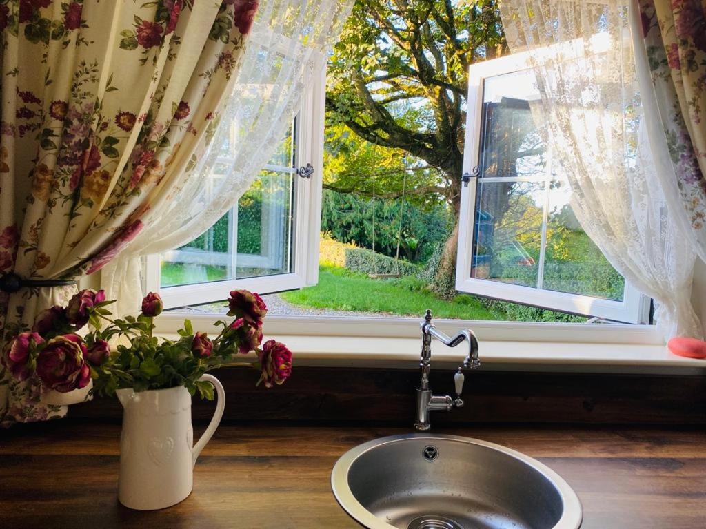 un fregadero con ventana y un jarrón con flores en Christie's Cottage, en Dungiven