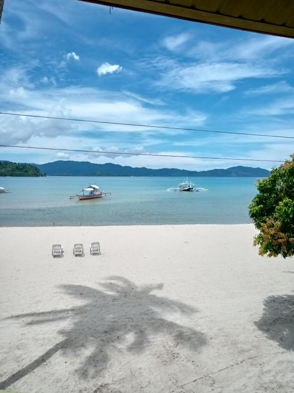 a view of a beach with two chairs and boats in the water at Greenviews Resort & Restaurant Port Barton in San Vicente