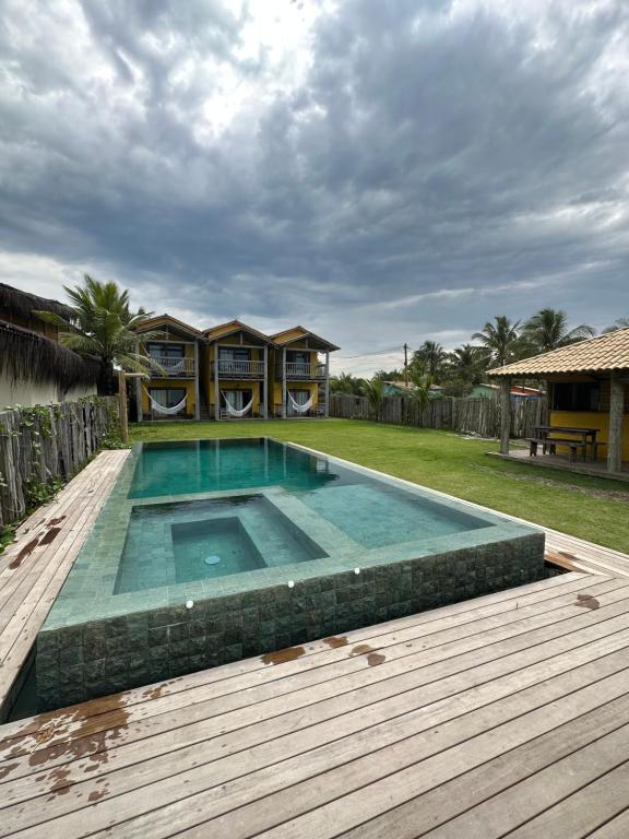 a swimming pool with a wooden deck and a house at Tamikuã Mar Pousada in Caraíva