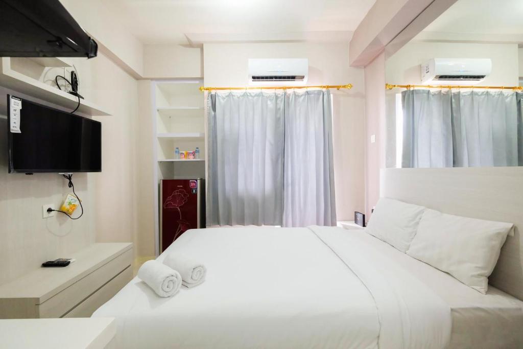 um quarto com uma cama branca e uma televisão em Green Pramuka city Harian by Dea roooms em Jakarta
