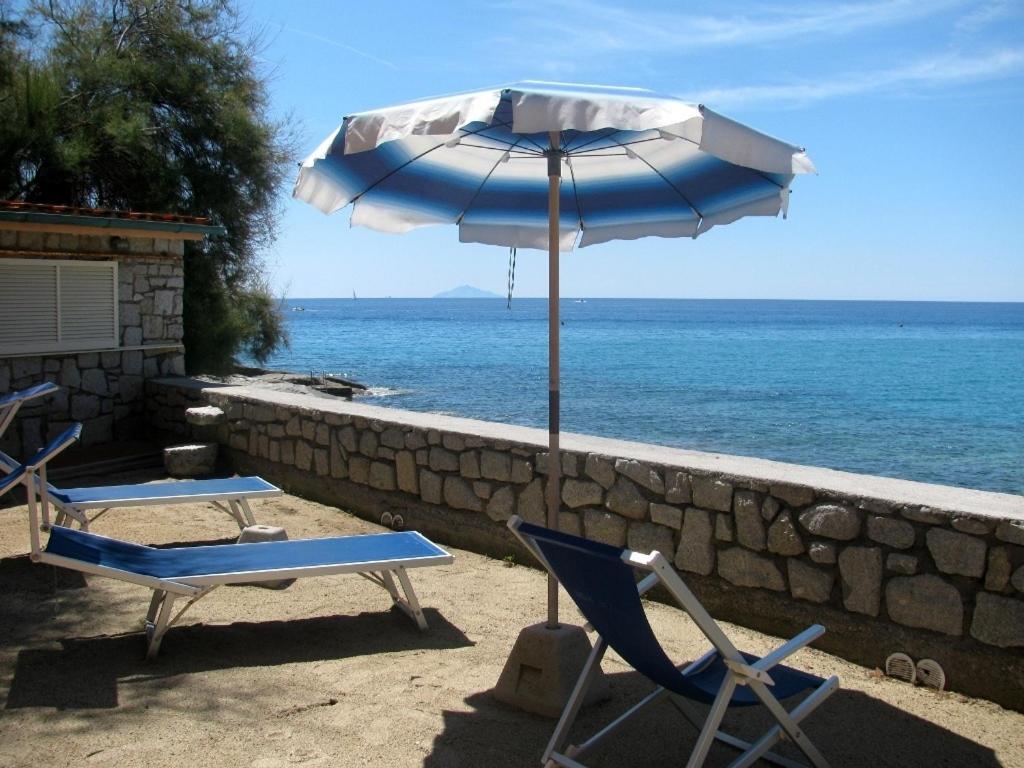 two chairs and an umbrella on a beach at Onda Su Onda Appartamenti in Seccheto