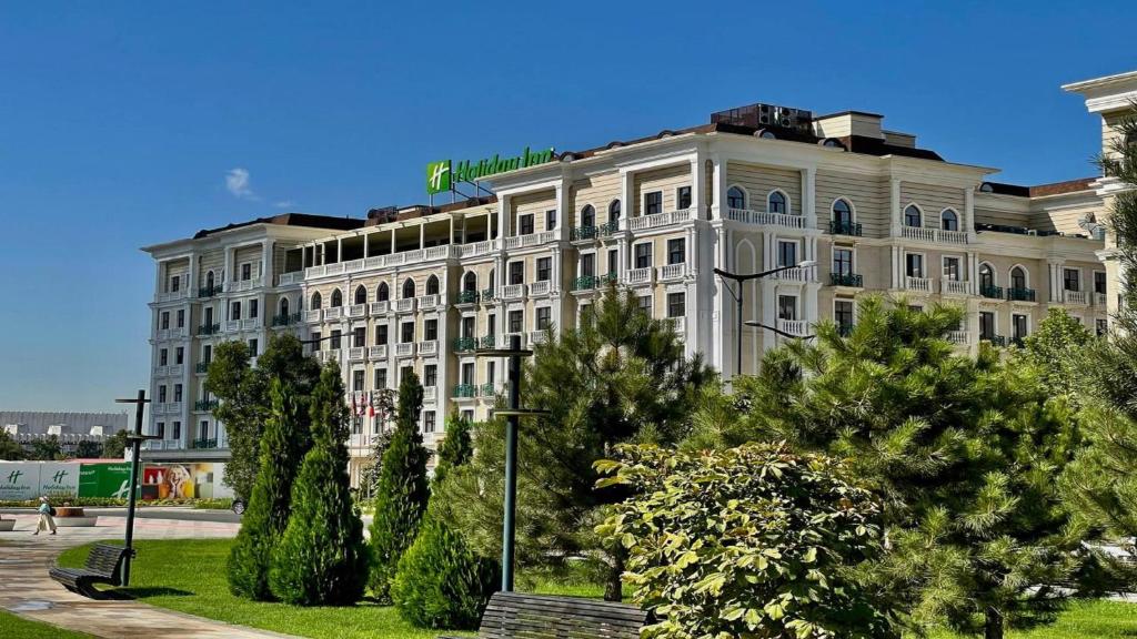 um grande edifício branco com árvores em frente em Holiday Inn Tashkent City, an IHG Hotel em Tashkent