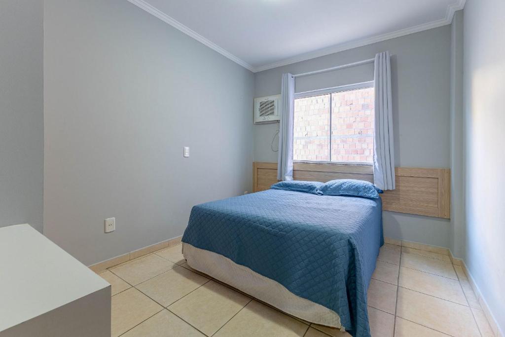 een slaapkamer met een bed met een blauwe deken en een raam bij Ideal para Casais, Loft na Praia de Bombinhas - 1 dorm in Bombinhas