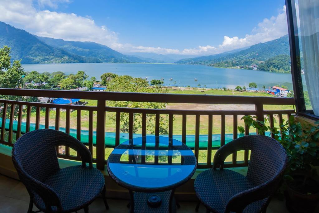 een tafel en stoelen op een balkon met uitzicht op een meer bij Hotel Fewa Camp in Pokhara