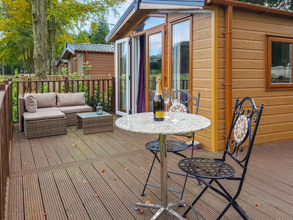 a table and chairs on a deck with a house at Glenbeagles Lodge in Dollar