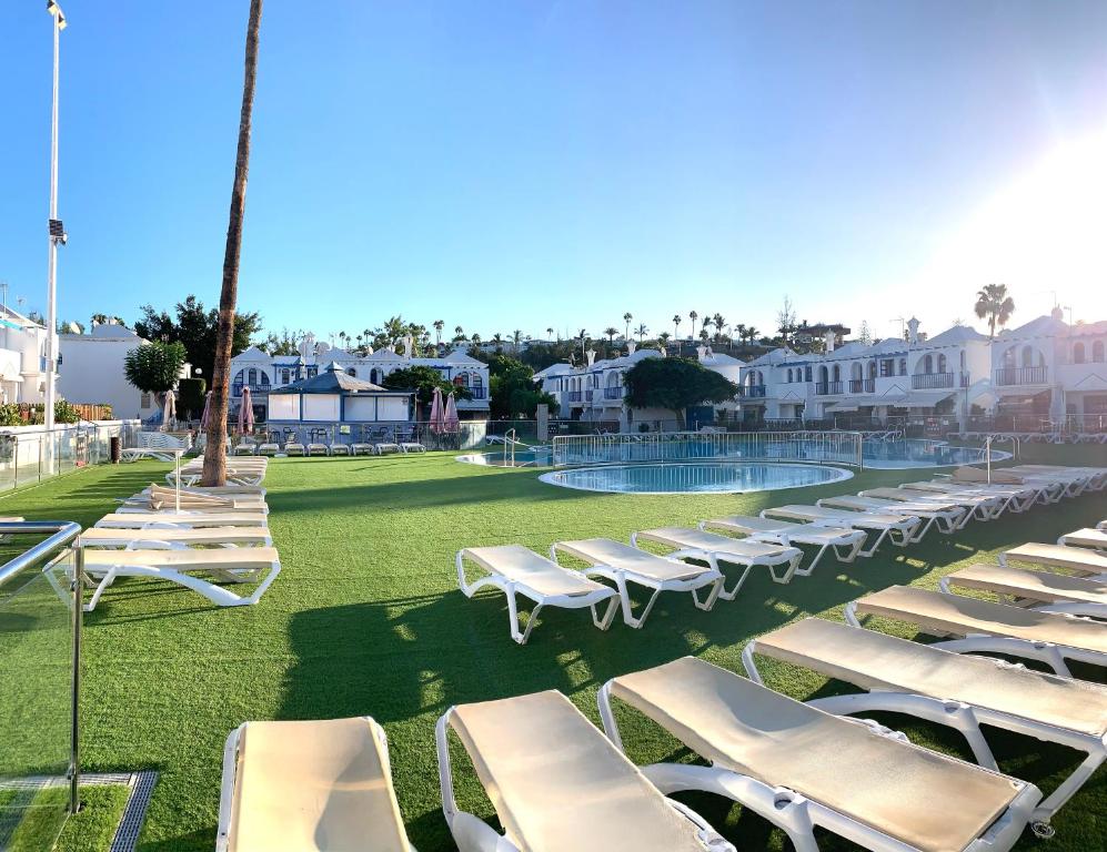 a row of chaise lounge chairs on a lawn with a pool at Bungalow Helena in Maspalomas