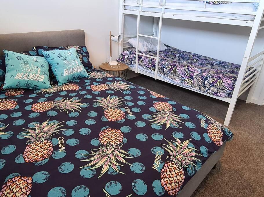 a bedroom with a bed and bunk beds with pineapple sheets at Coastal Palms - relax by the golf course in Normanville