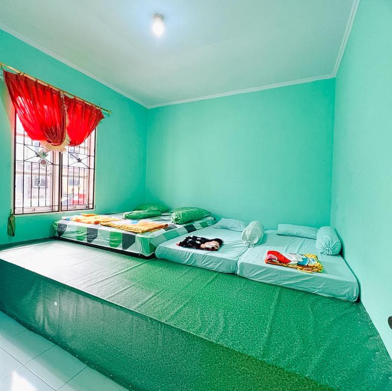 2 Betten in einem Zimmer mit blauen Wänden und einem Fenster in der Unterkunft VILLA BUKIT MAS BERASTAGI DEPAN MIKIE FUNLAND in Berastagi