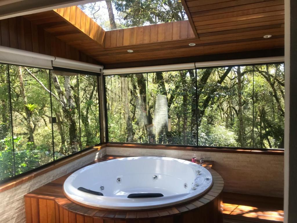 a large bath tub in a room with a large window at Chalés Recanto das Montanhas in Monte Verde