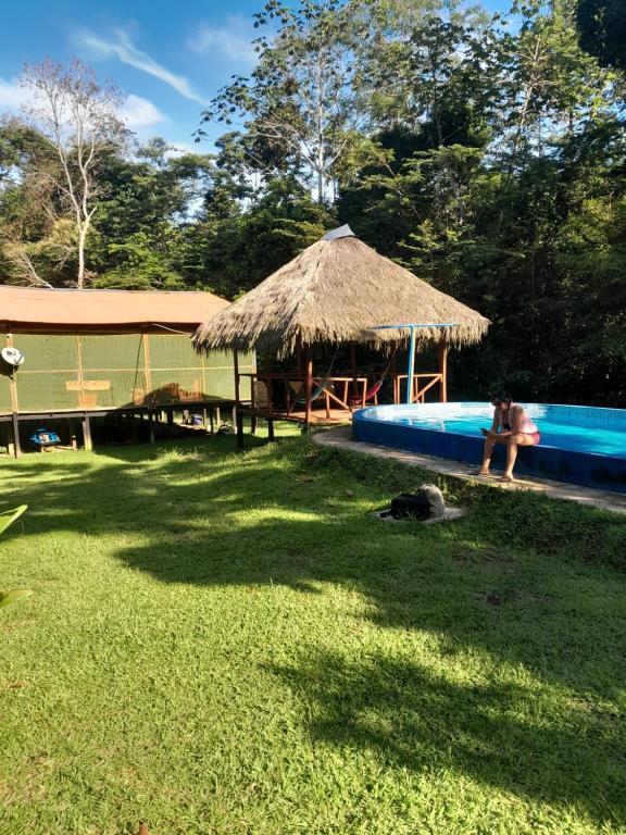 a person sitting next to a swimming pool with a hut at Jungle Explorer Lodge in Mazán