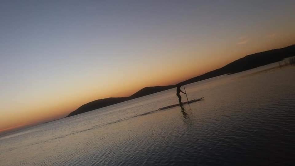 eine Person, die bei Sonnenuntergang am Strand im Wasser steht in der Unterkunft Cabana recantodosamigositapua praia dos passarinhos itapua in Viamão