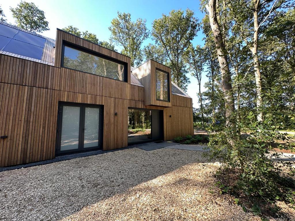 a house with a wooden facade with a tree at NIEUW Eco design bosvilla met sauna en xl tuin in Wateren