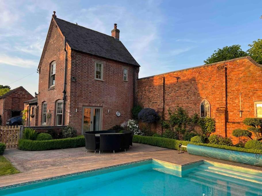 a brick building with a swimming pool in front of a house at The Cottage, Orgreave Estate in Yoxall