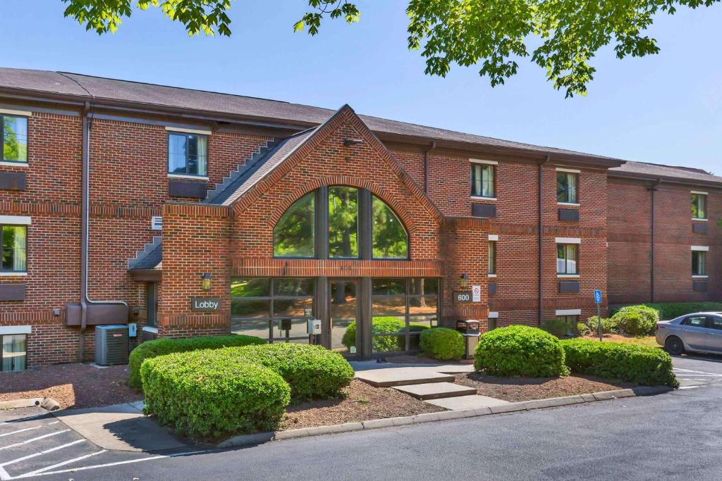 a brick building with bushes in front of it at Extended Stay America Suites - Raleigh - Cary - Harrison Ave in Cary