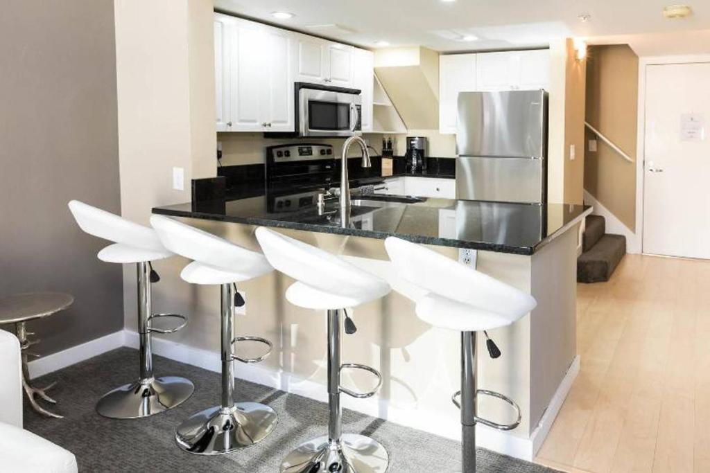 a kitchen with white stools and a black counter top at Space Needle Downtown Modern Top Story Penthouse in Seattle