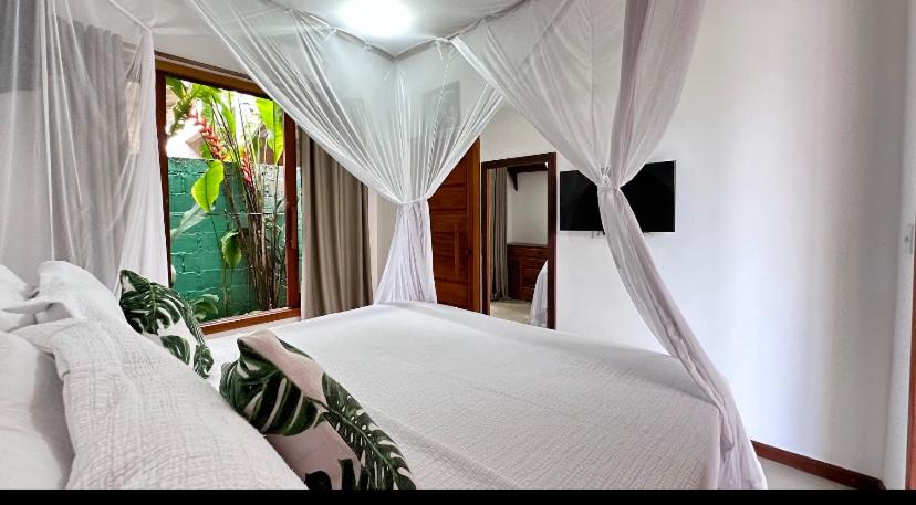 a bedroom with a white bed and a window at CASA SIMONI Trancoso in Trancoso