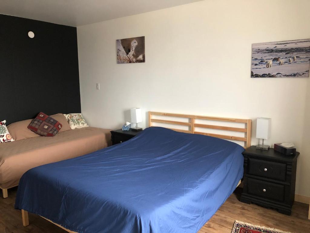 チャーチルにあるInukshuk Roomsのベッドルーム1室(ベッド2台、青いシーツ、ランプ2つ付)