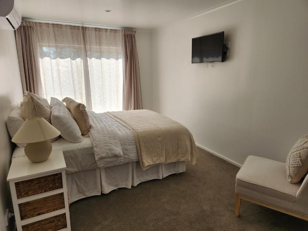 a bedroom with a bed and a window and a chair at Guest House on Guthrie in Havelock North
