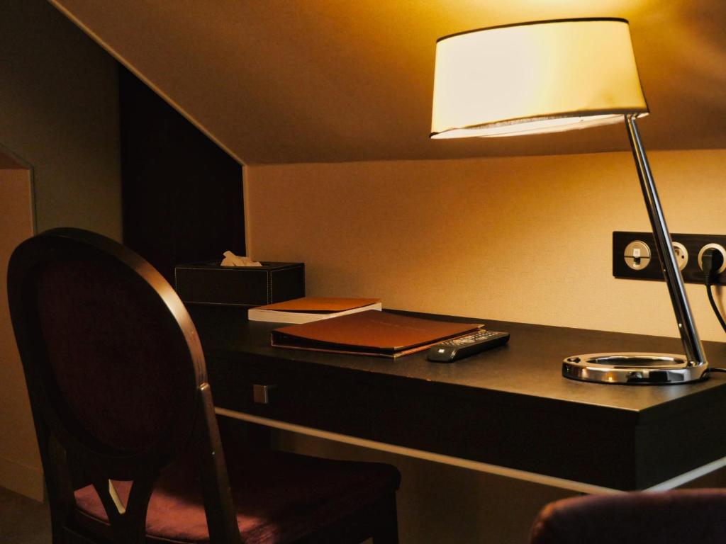 a desk with a lamp and a book on it at Amicitia - Hôtel &amp; Restaurant in LʼIsle-Adam