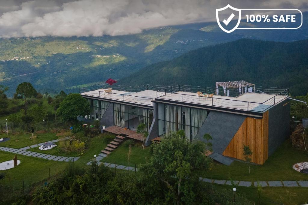 a house on a hill with mountains in the background at SaffronStays Glasshouse Celeste, Ranikhet - luxurious glass villa with breathtaking views in Bhatrojkhan