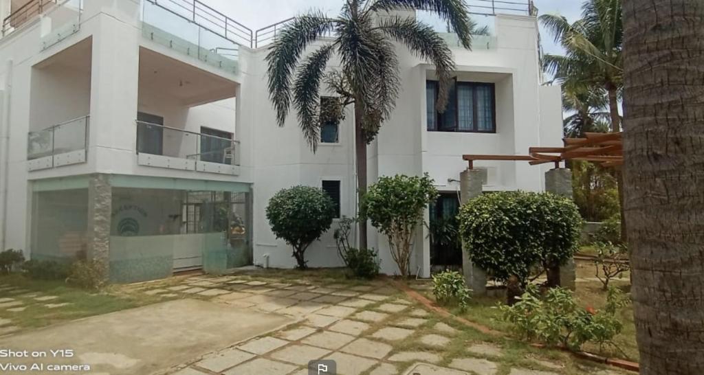 a white house with a palm tree in front of it at Beach wave villa in Tirupporūr