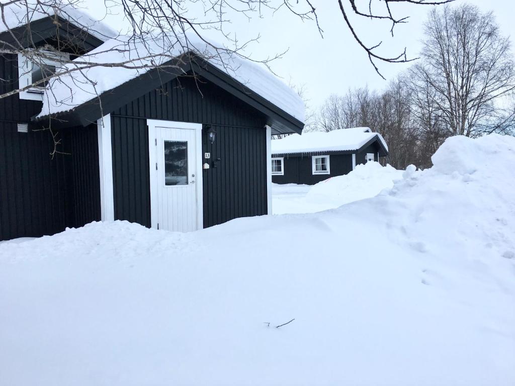 um edifício preto com uma porta branca na neve em Hyttgårdens stugby i Huså, Åre kommun em Järpen