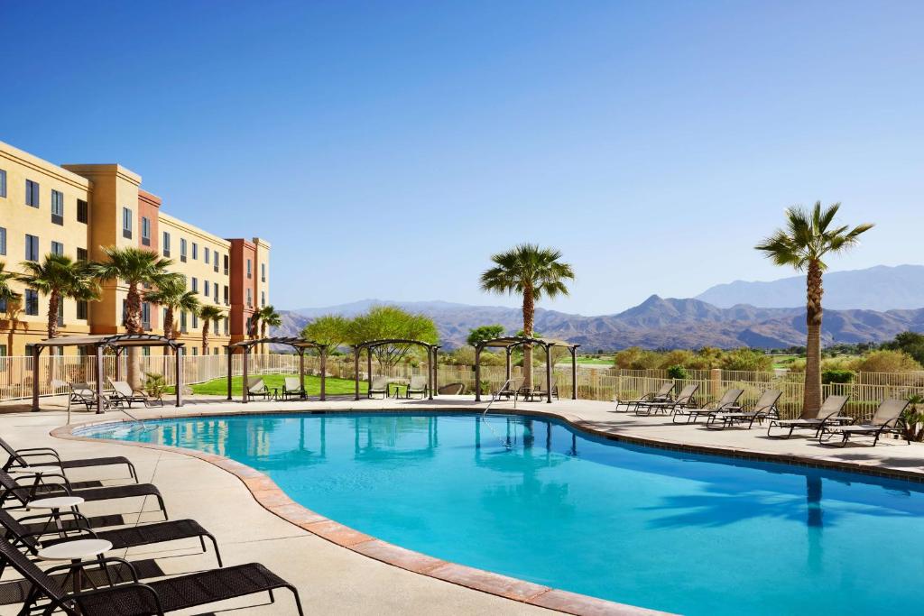 einen großen Pool mit Stühlen und Palmen in der Unterkunft Homewood Suites by Hilton Cathedral City Palm Springs in Cathedral City