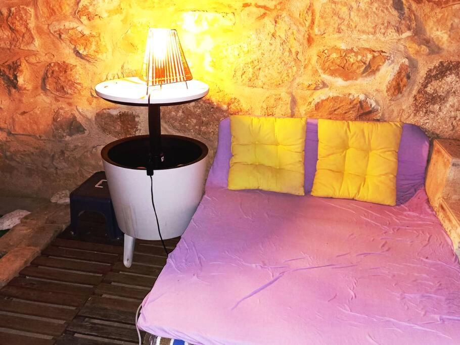 a purple bed with a lamp next to a stone wall at MiniCasa con vistas a las Hoces del río Riaza. in Montejo de la Vega de la Serrezuela