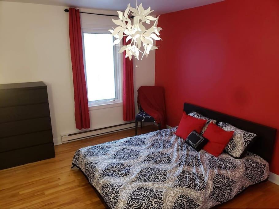 una camera da letto con un letto con pareti rosse e un lampadario a braccio di Un appartement chaleureux décoré avec bon goût. a Saint-Jean-sur-Richelieu