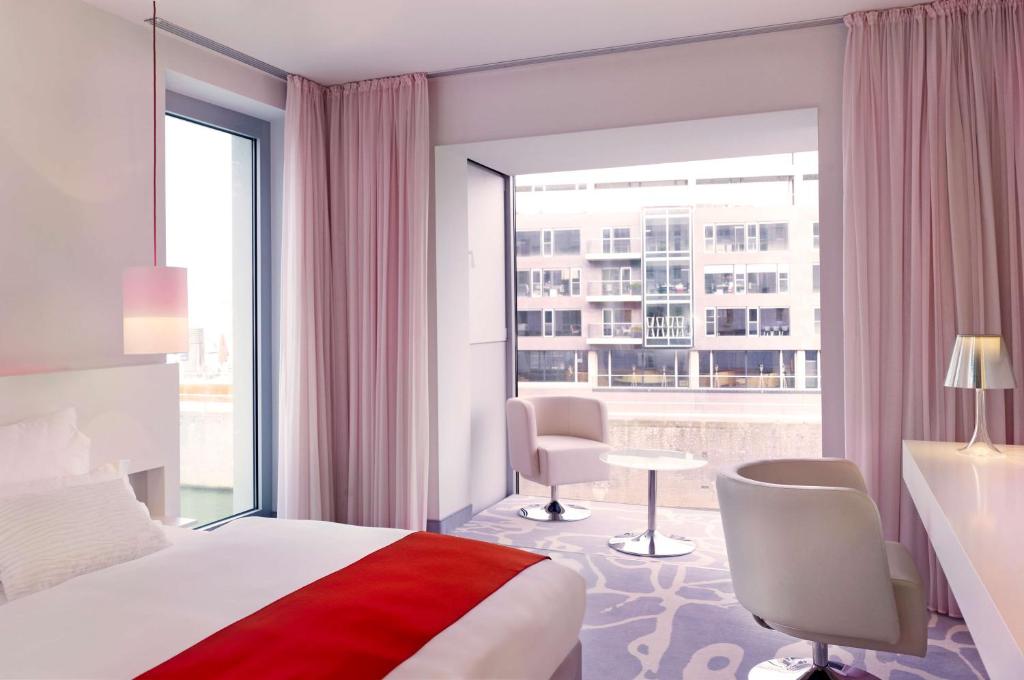 a hotel room with a bed and a large window at art'otel cologne, Powered by Radisson Hotels in Cologne