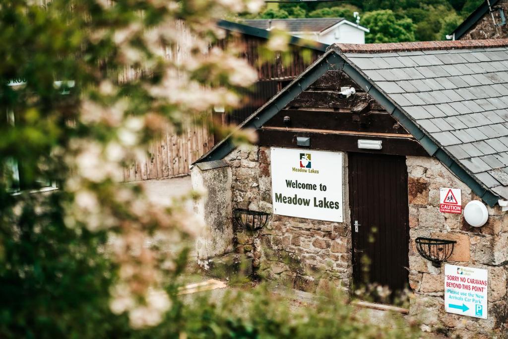 una señal en el lateral de un edificio con una señal de bienvenida a los lagos de Melbourne en Meadow Lakes Holiday Park, en Grampound