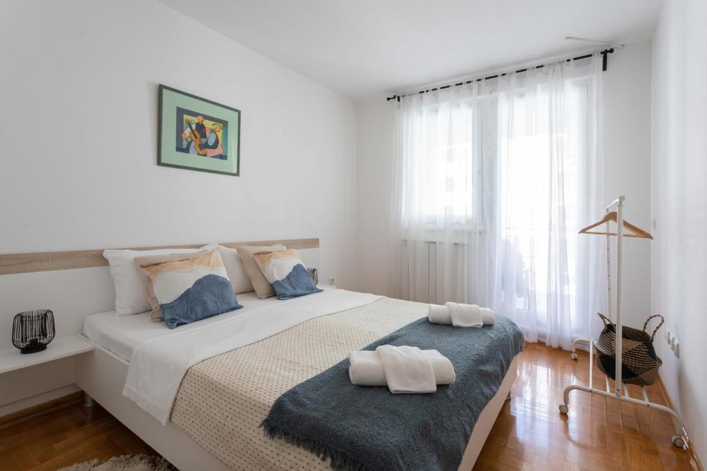 - une chambre blanche avec un grand lit et une fenêtre dans l'établissement Sunny 1BDR with Balcony & Parking, à Zagreb