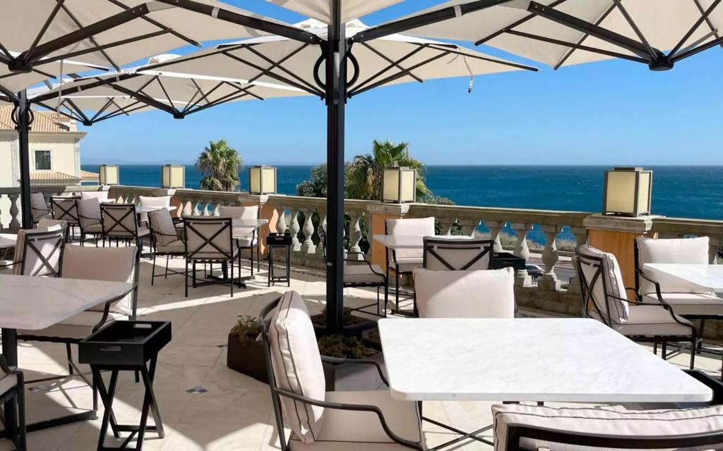 a restaurant with white tables and chairs and the ocean at Grande Real Villa Itália Hotel & Spa in Cascais