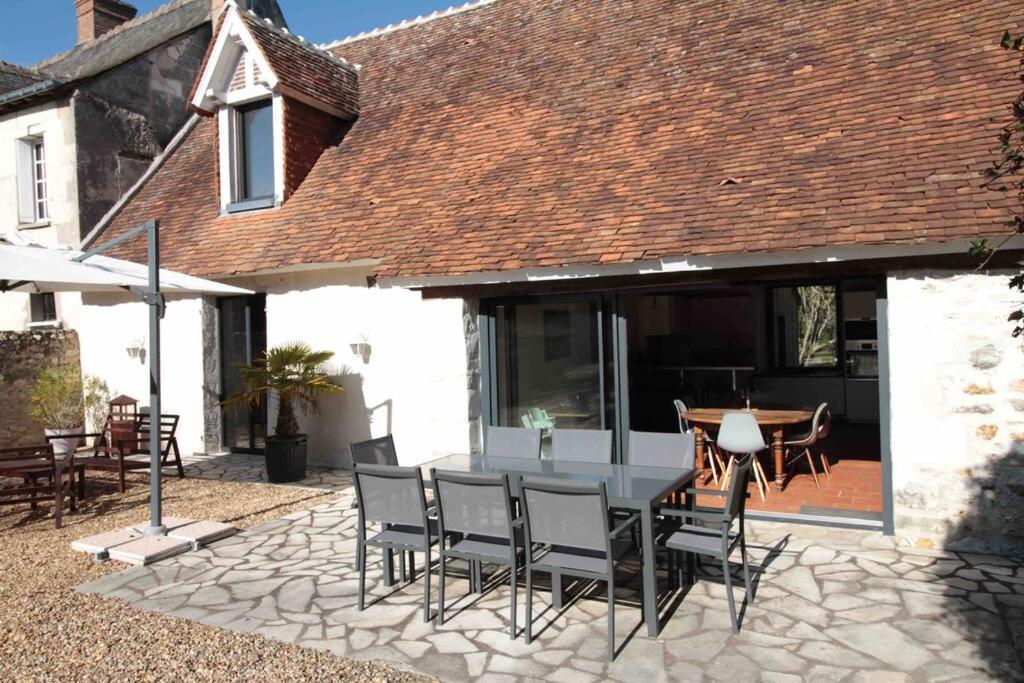 een patio met een tafel en stoelen en een huis bij La Pidellerie bord de Cher-Châteaux de la Loire in Véretz