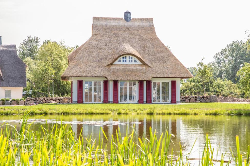 a house with a thatched roof reflected in a pond at Ferienhaus Haubenlerche 27 in Fuhlendorf