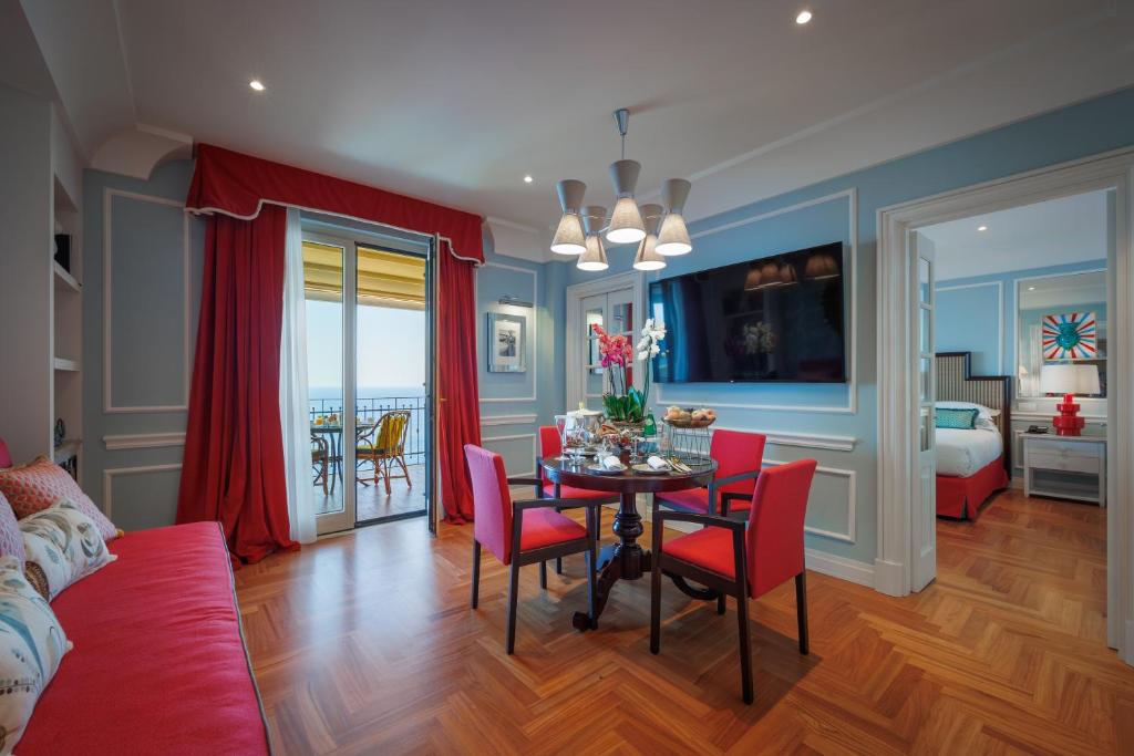 a living room with a dining room table and red chairs at Grand Hotel San Pietro Taormina in Taormina
