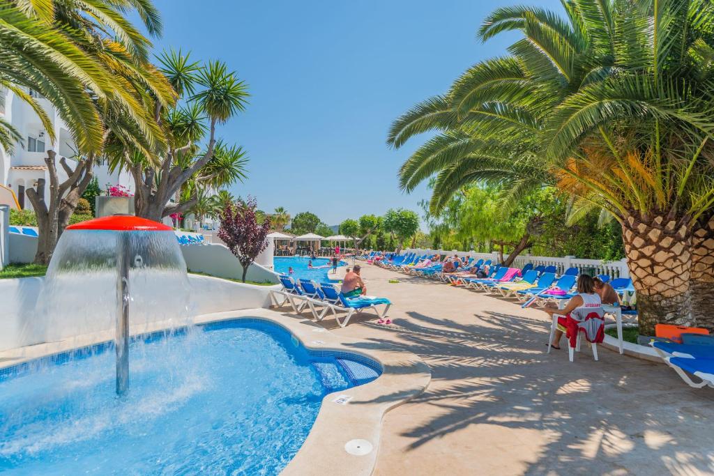 una piscina en un complejo con palmeras y gente sentada en sillas en Aparthotel Holiday Center en Santa Ponsa