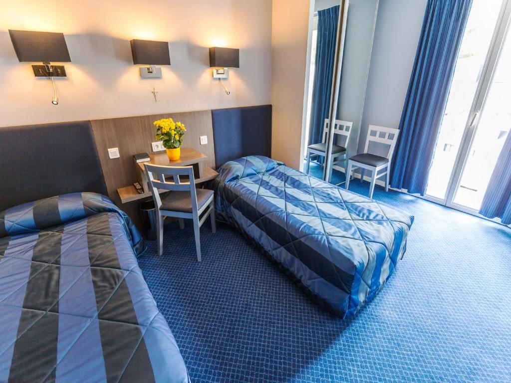 ルルドにあるHôtel Irlandeのベッド2台、テーブルと椅子が備わるホテルルームです。