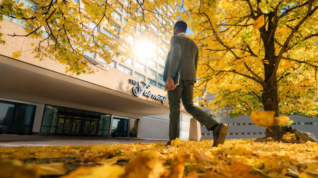 Un uomo che cammina tra le foglie di fronte a un edificio di Fairmont Winnipeg a Winnipeg