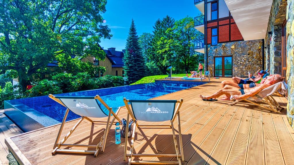 - deux personnes assises sur des chaises longues sur une terrasse à côté d'une piscine dans l'établissement Apartament Green Resort B15 z Basenem, Sauną, Jacuzzi, Siłownią-5D Apartamenty, à Szklarska Poręba